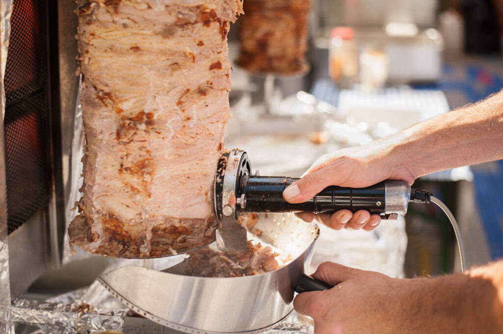 Hands of the Cook that with electric knife cut the doner kebab.